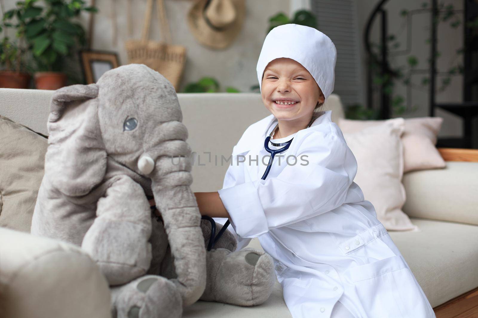 Adorable child dressed as doctor playing with toy elephant, checking its breath with stethoscope