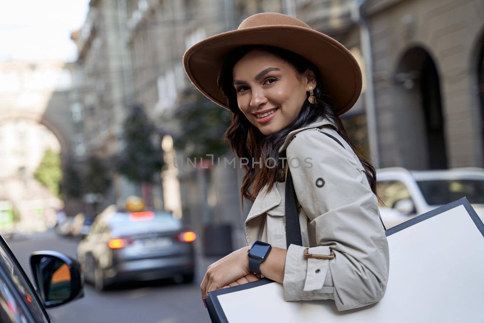 Feeling happy after shopping. Portrait of a young beautiful caucasian woman in hat with shopping bag looking at camera and smiling while standing on the city street by friendsstock