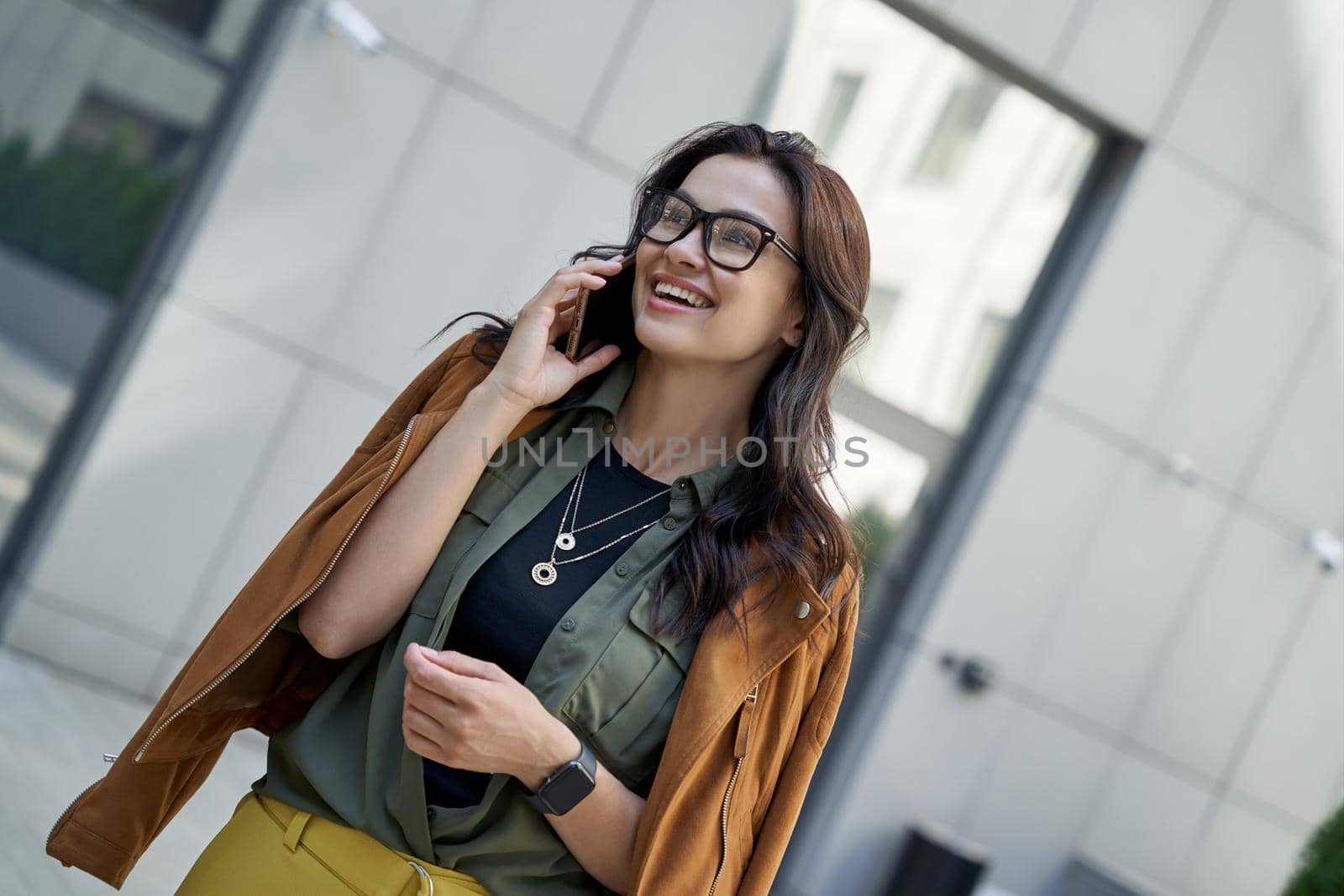 Enjoying nice talk. Young beautiful and stylish woman talking on smartphone with friend and smiling while walking on the city street by friendsstock