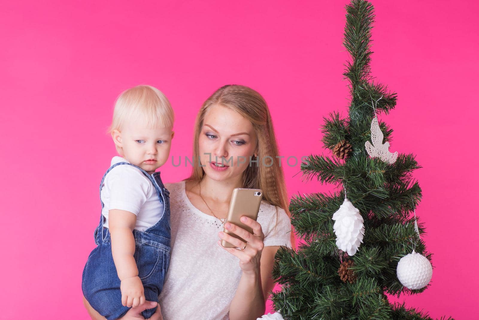 Mother and little daughter taking a selfie near Christmas tree.