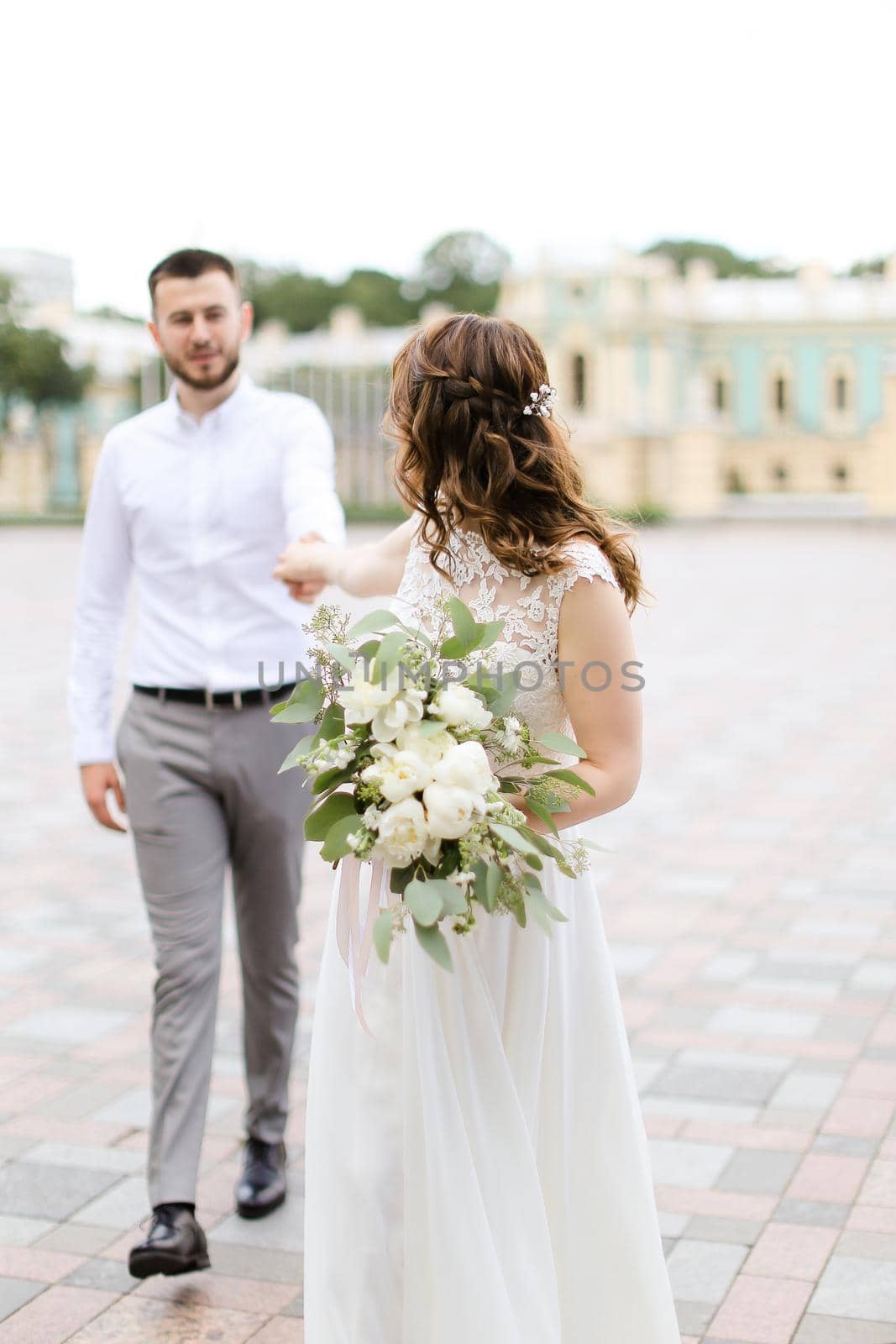 Caucasian bride walking with groom and bouquet of flowers in city. by sisterspro