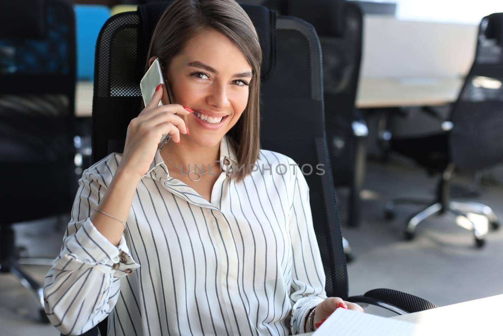 Attractive business woman talking with collegues on the mobile phone while sitting in the office desk.