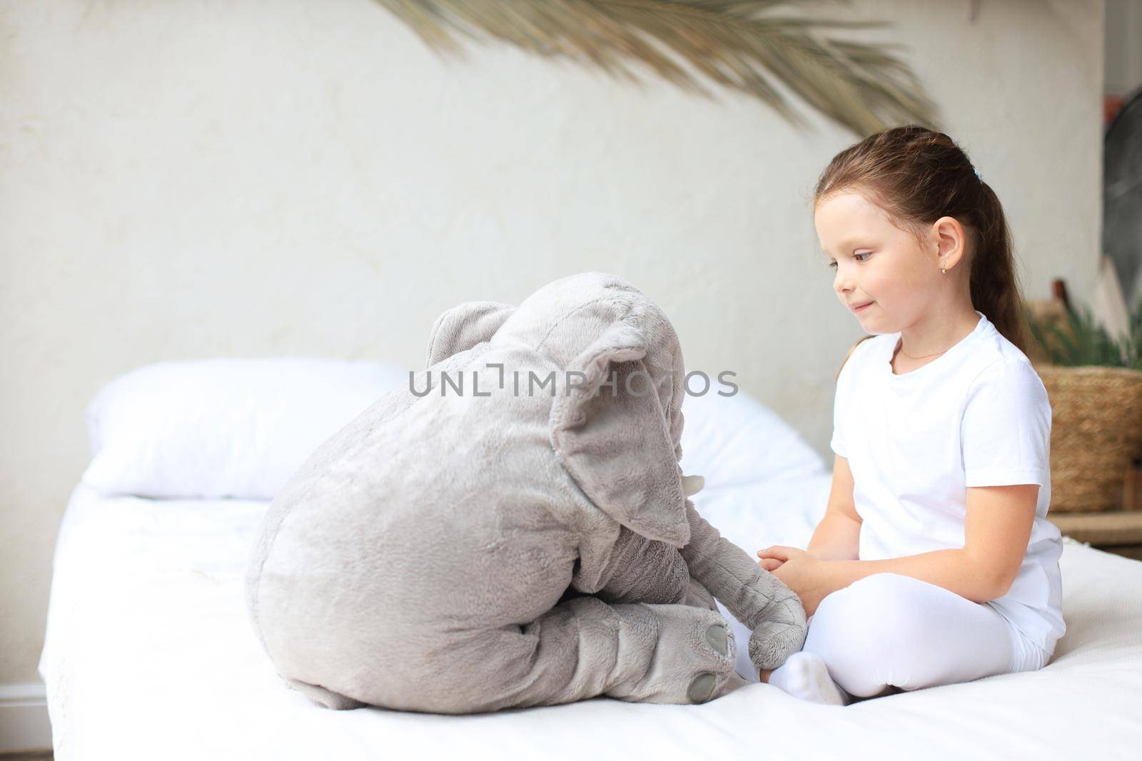 Sweet little girl sitting on her bed at home with toy elephant