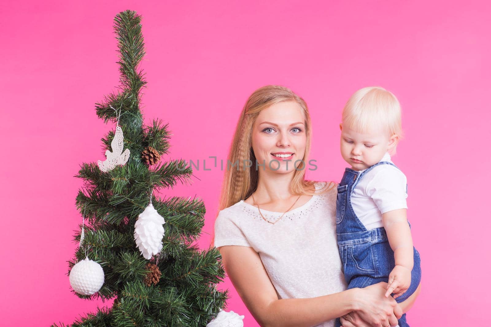 Christmas, holidays and people concept - woman and her kid near christmas tree over pink background.
