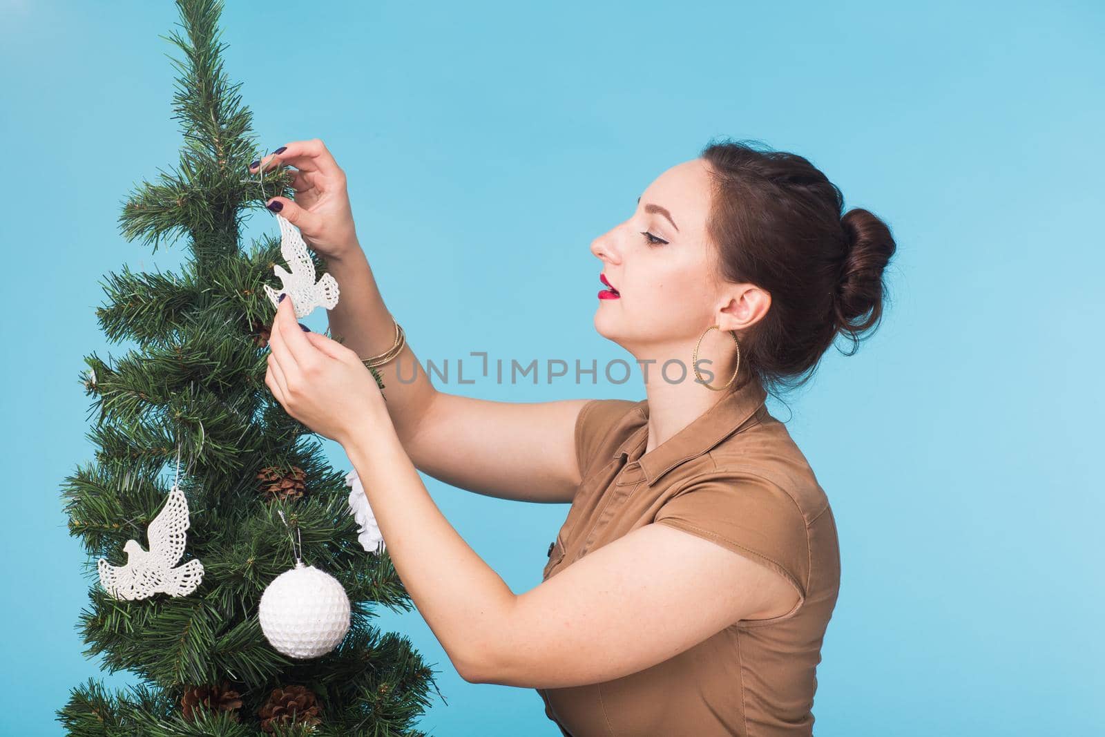 People, holidays and christmas concept - woman decorating christmas tree on blue background.