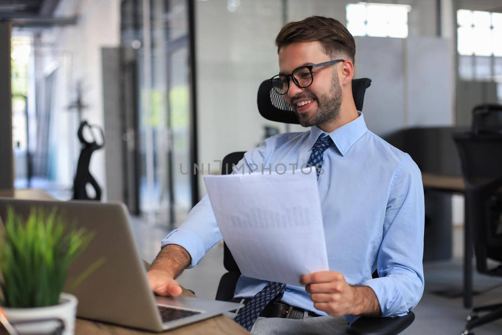 Young man is working with papers while sitting in the office. Successful entrepreneur is studying documents with attentive and concentrated look.