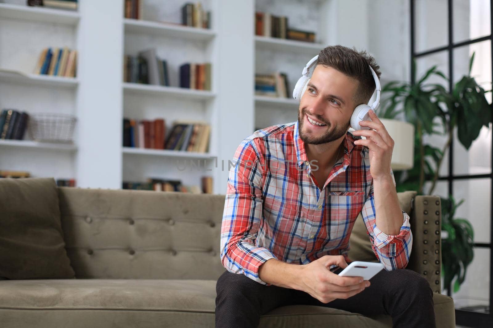 Attractive young man relaxing on a couch at home and using mobile phone for cheking social nets