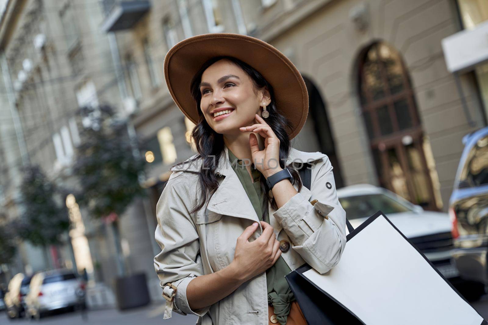 Fashion girl. Portrait of a young beautiful stylish woman in hat with shopping bag looking aside and smiling while standing on the city street by friendsstock