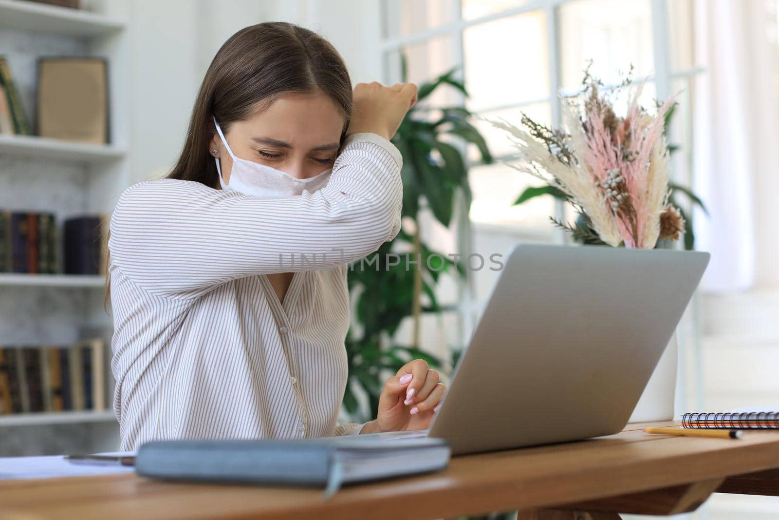 Young businesswoman in a medical protective mask works from home at the laptop during self-isolation and quarantine