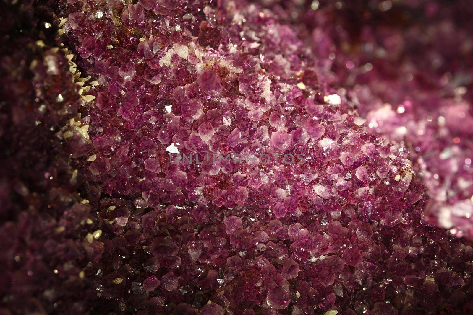 Close up background of vivid purple amethyst crystals geode bright lit in the dark