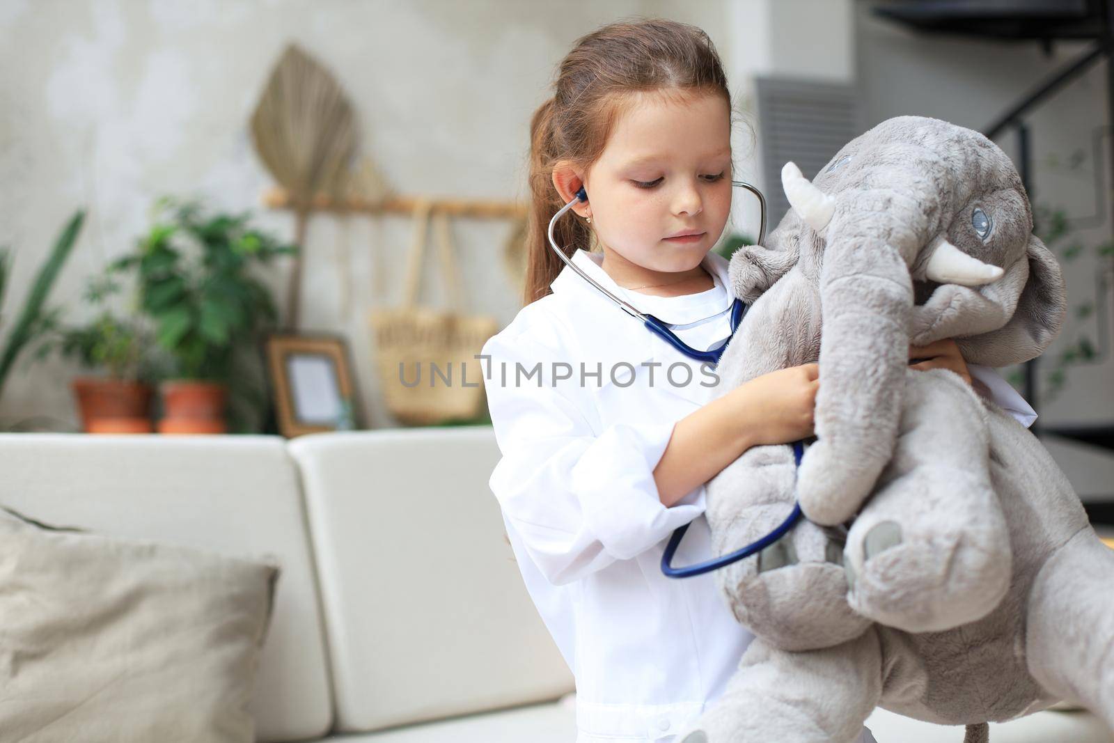 Adorable child dressed as doctor playing with toy elephant, checking its breath with stethoscope