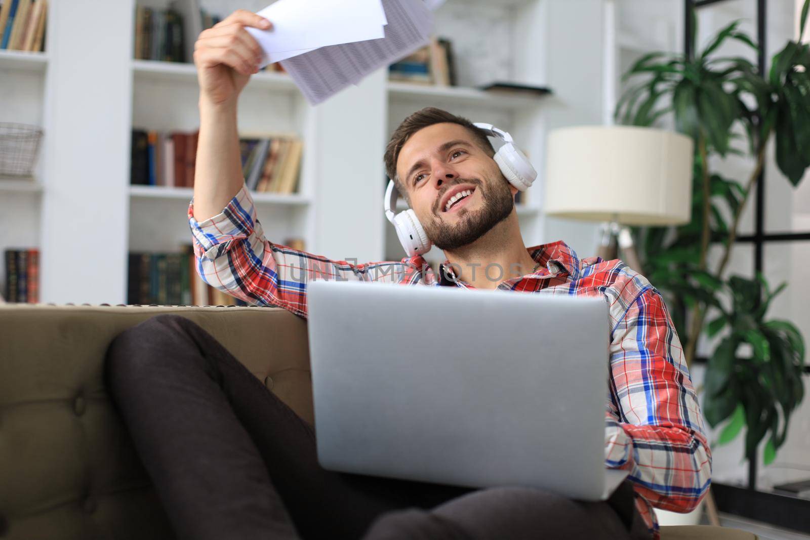 Young tired freelancer in casualwear sitting on sofa in front of laptop