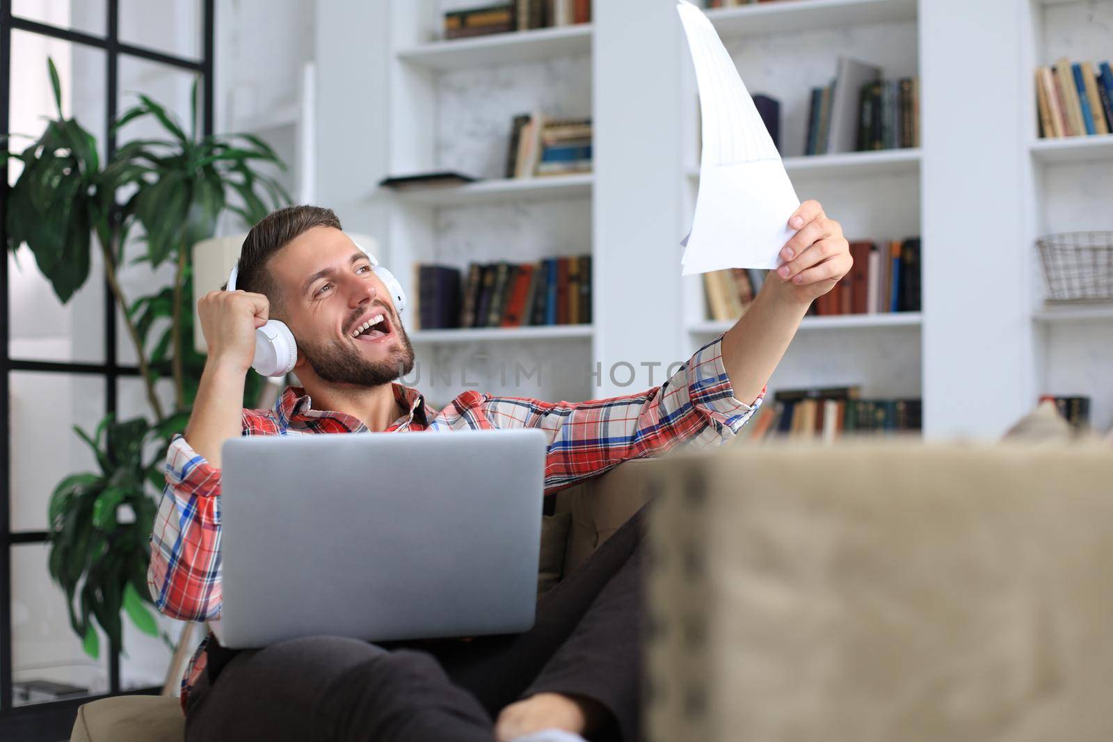 Concentrated young freelancer businessman sitting on sofa with laptop, working remotely online at home