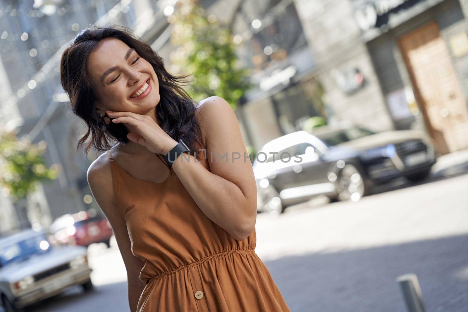 Perfect summer day. Portrait of a young attractive happy woman wearing dress keeping eyes closed and smiling while walking on the city streets on a sunny day by friendsstock