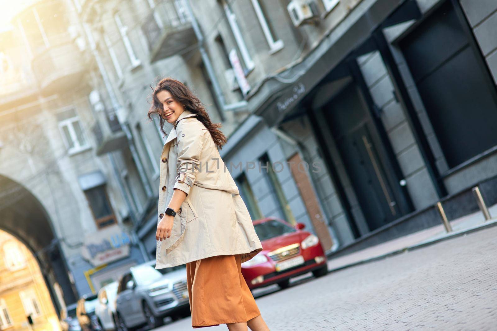 Perfect weather for walking. Young happy stylish caucasian woman wearing grey coat looking at camera and smiling while standing on the city street, posing outdoors. Beautiful people, fashion concept