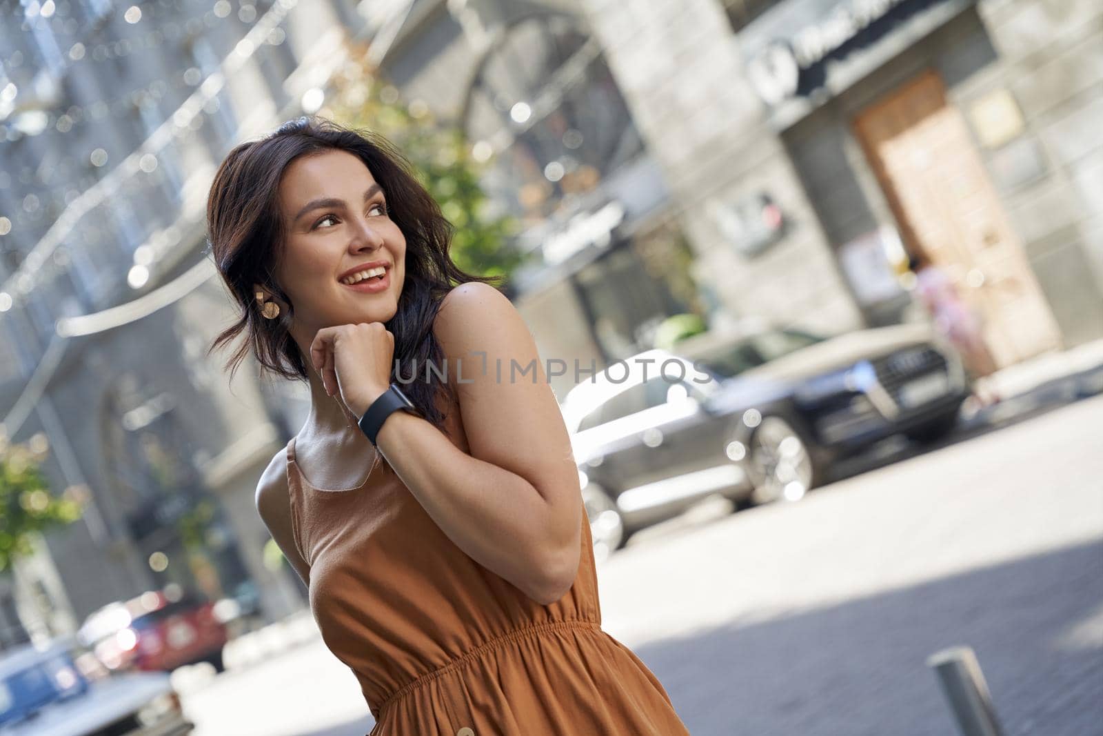 Portrait of a young attractive happy woman wearing summer dress looking aside and smiling while walking on the city streets on a sunny day by friendsstock