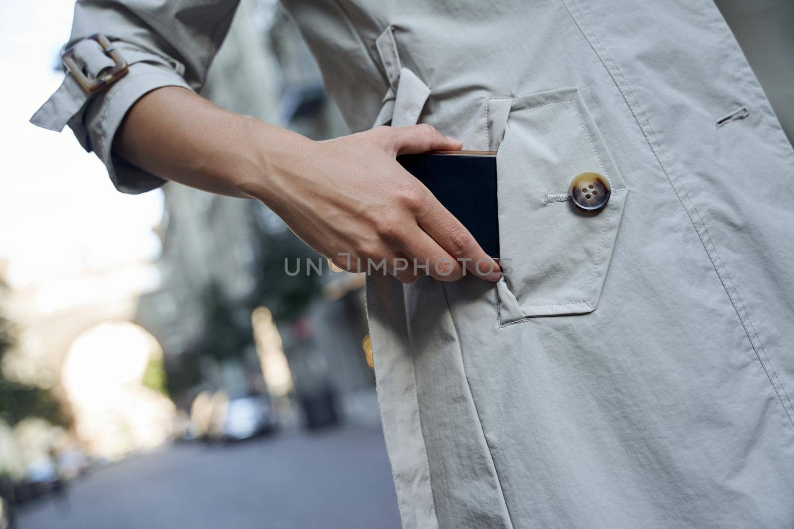 Cropped shot of a woman in grey coat putting her smartphone in pocket while standing outdoors by friendsstock