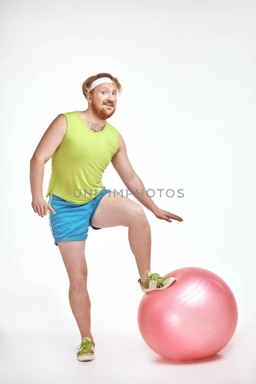 Red haired, bearded, plump man put his leg to a fitness ball by friendsstock