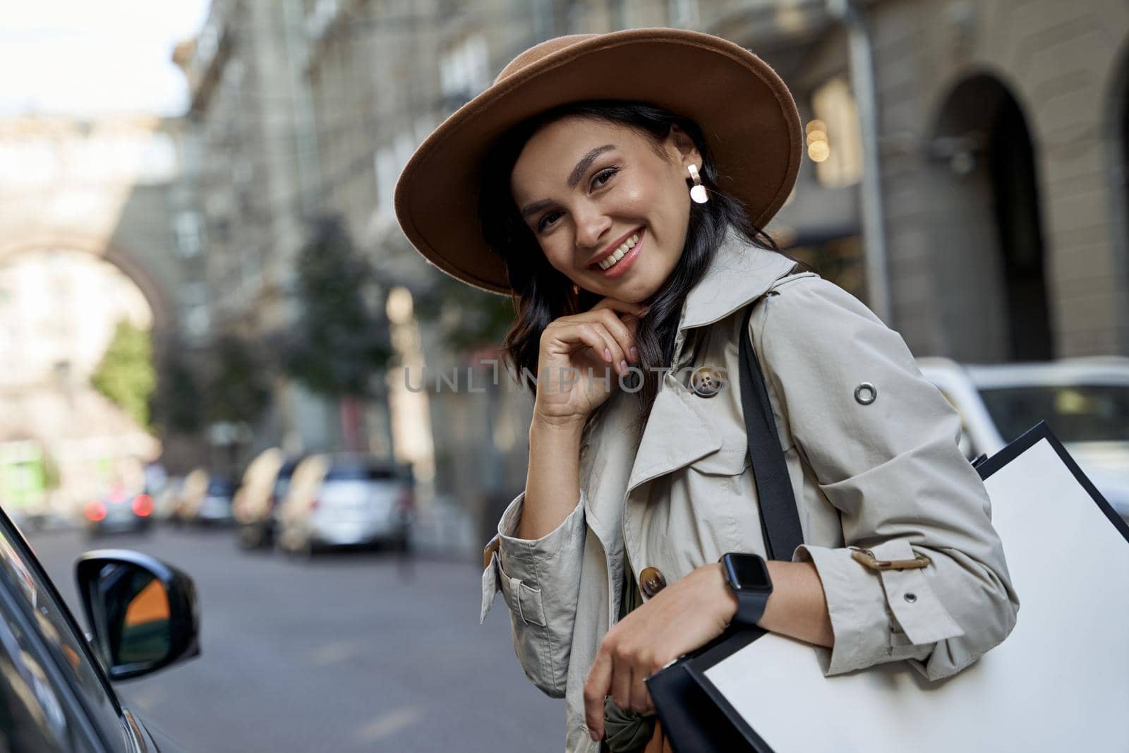 Shopping makes me feel good. Portrait of a young beautiful and happy caucasian woman in hat with shopping bag looking at camera and smiling while standing on the city street. Fashion, people lifestyle