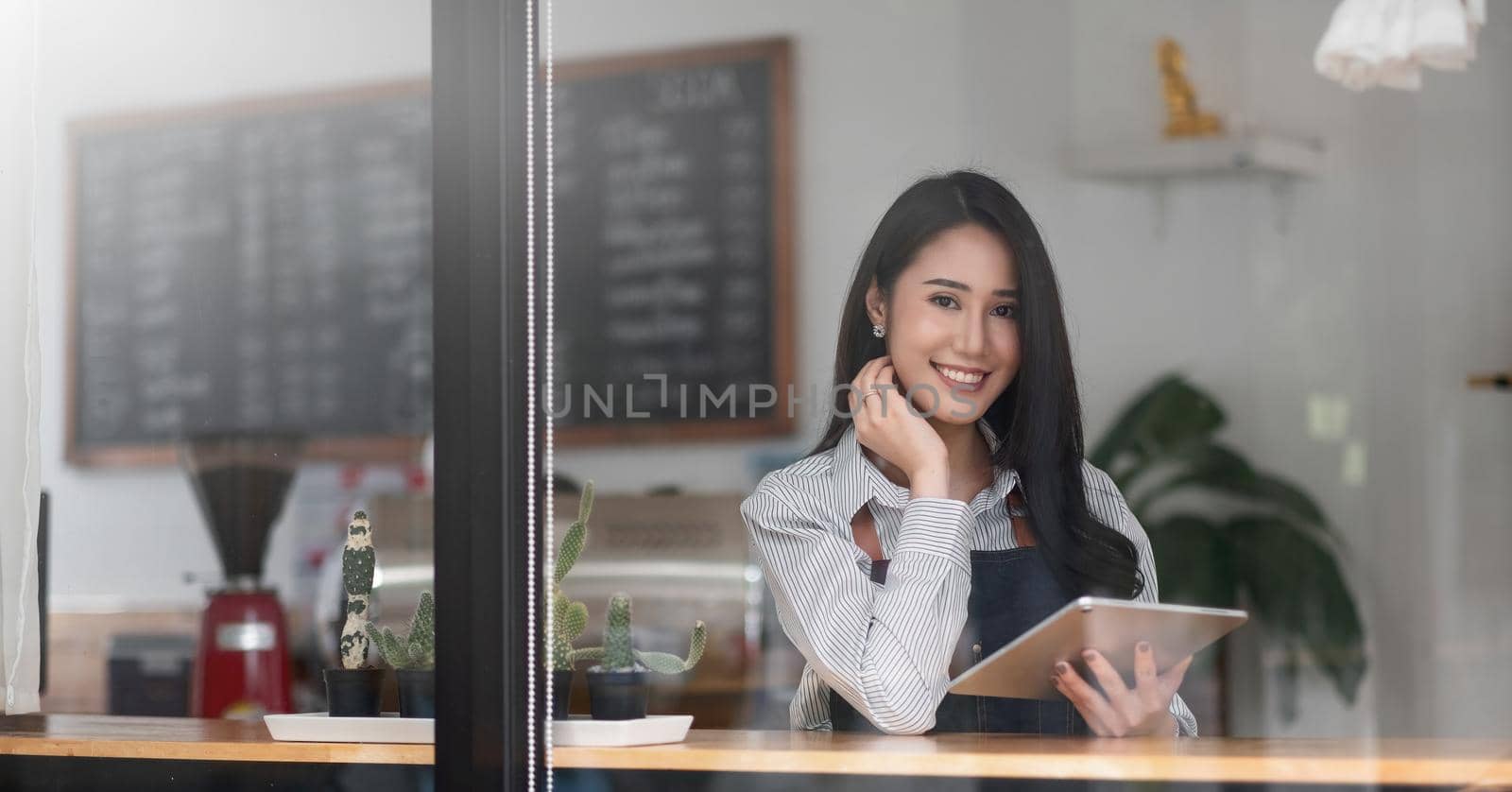 Cheerful young asian woman owner holding digital tablet while standing in her cafe, young entrepreneur conceptual.