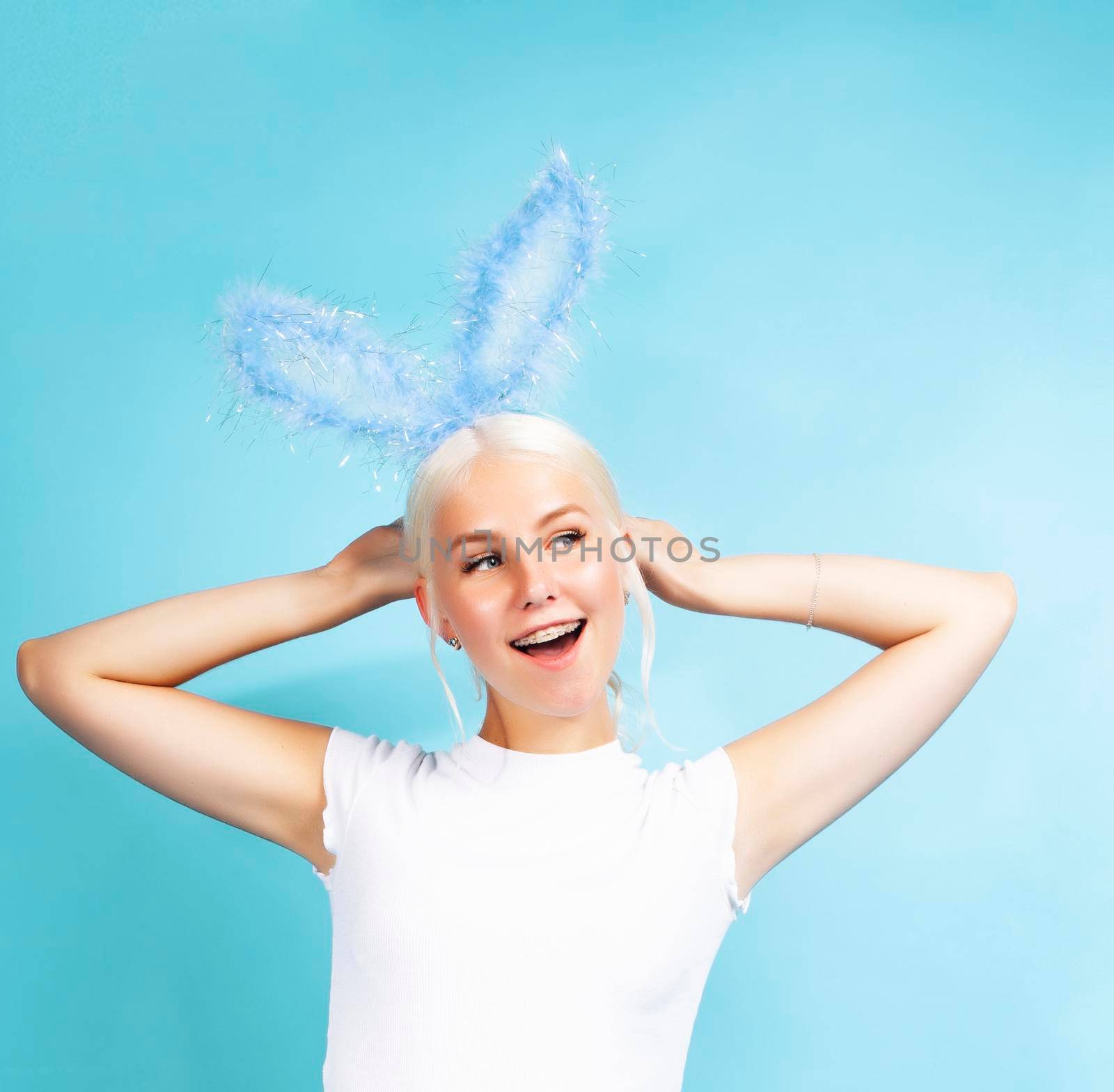 young pretty blond girl with rabbit ears posing cheerful on blue background, lifestyle people concept close up