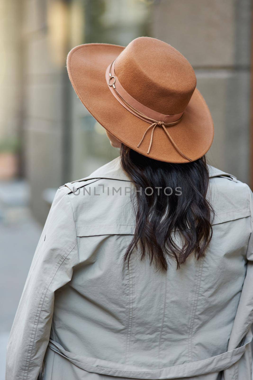 Rear view of a stylish woman wearing grey coat and hat standing on the city street, walking on warm autumn day. Fashion and beautiful people concept