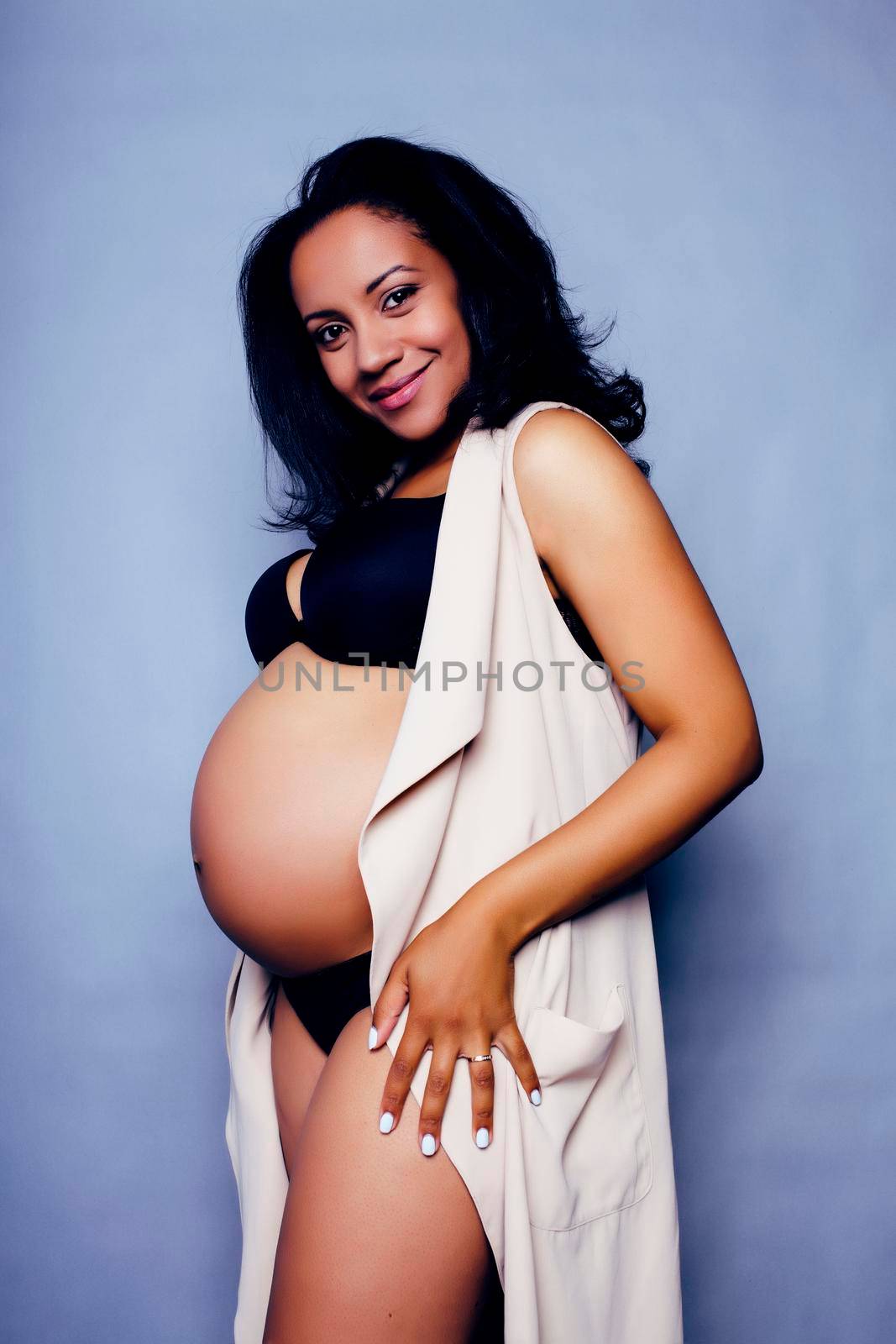 young pretty african american woman pregnant happy smiling, posing on blue background, lifestyle people concept copyspace close up