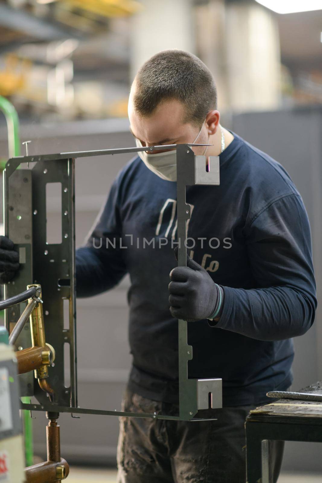a uniformed worker working in a modern metal production and processing factory assembles parts of a new machine on his desk. High quality photo