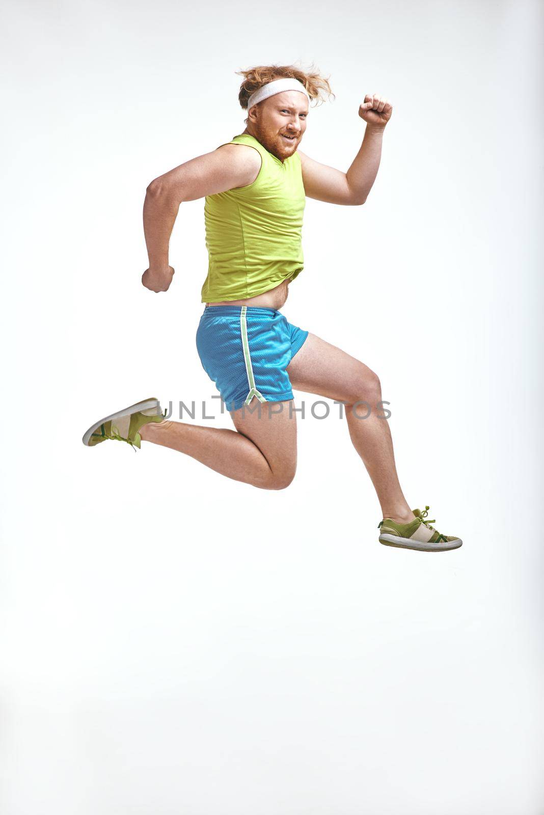 Funny picture of red haired, bearded, plump man on white background. Man wearing sportswear