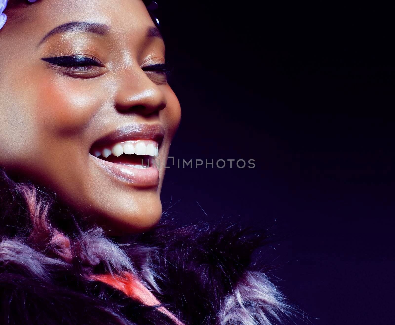 young pretty african american woman in spotted fur coat and flowers on head smiling on black background, fashion people concept by JordanJ