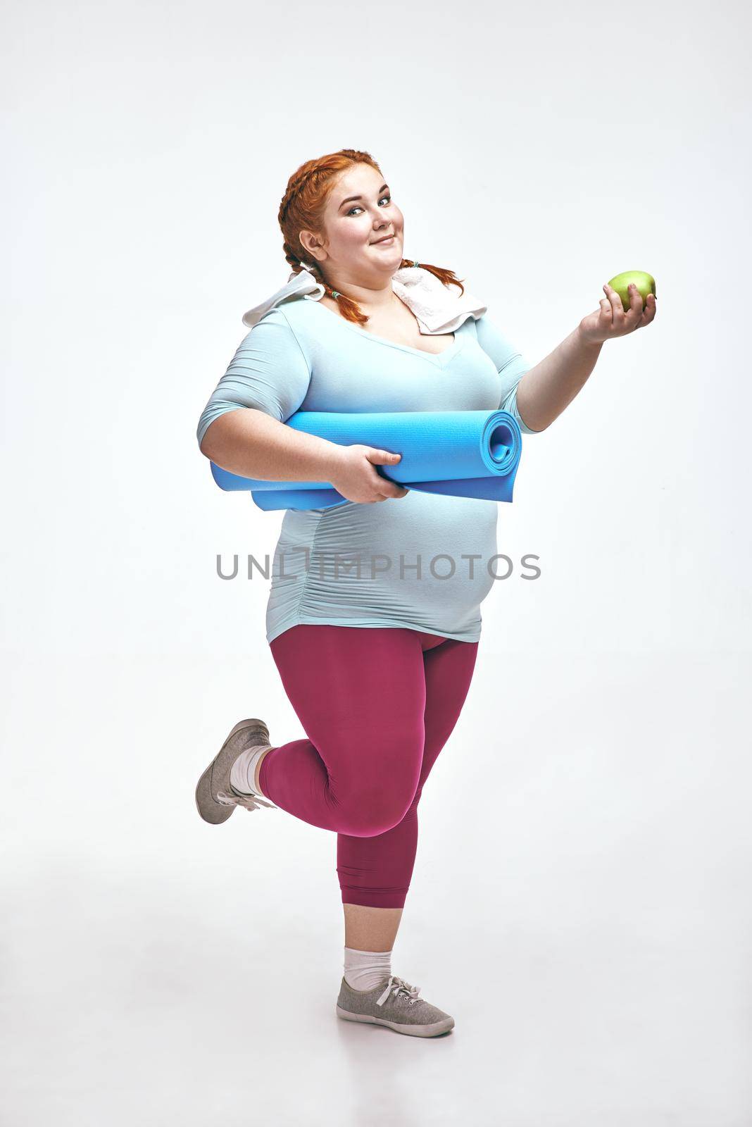 Funny picture of amusing, red haired, chubby woman on white background. Woman holding a mat.