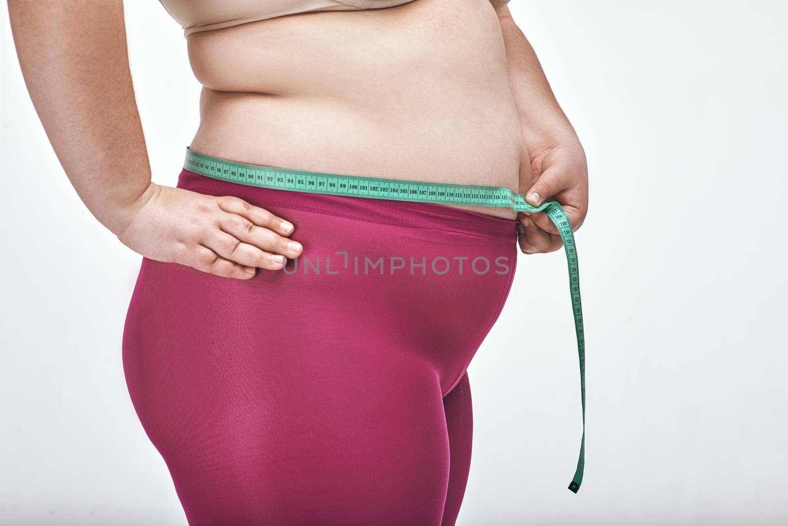 Picture of chubby woman on white background. Woman is measuring her belly