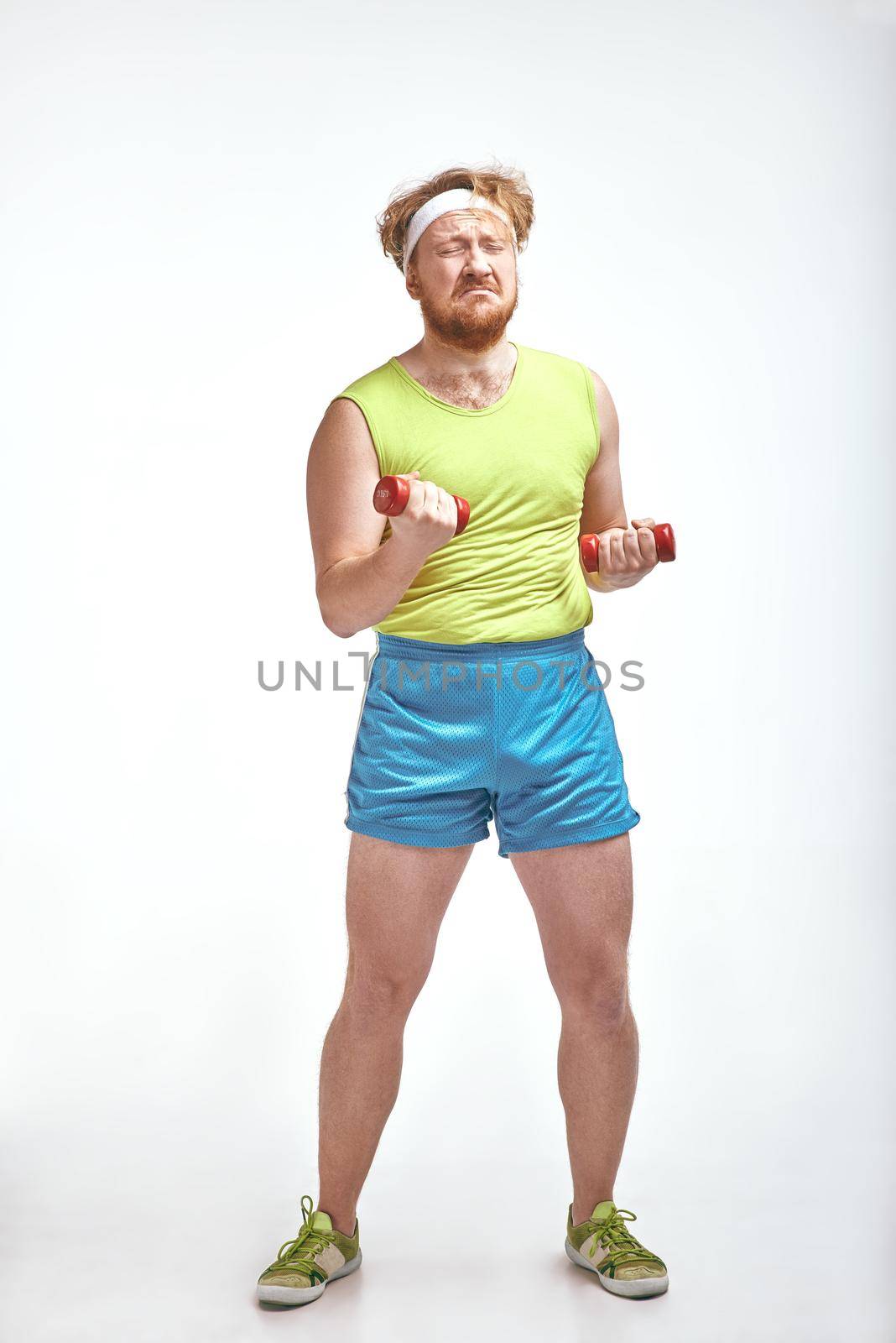 Red haired, bearded, plump man is holding the dumbbells by friendsstock