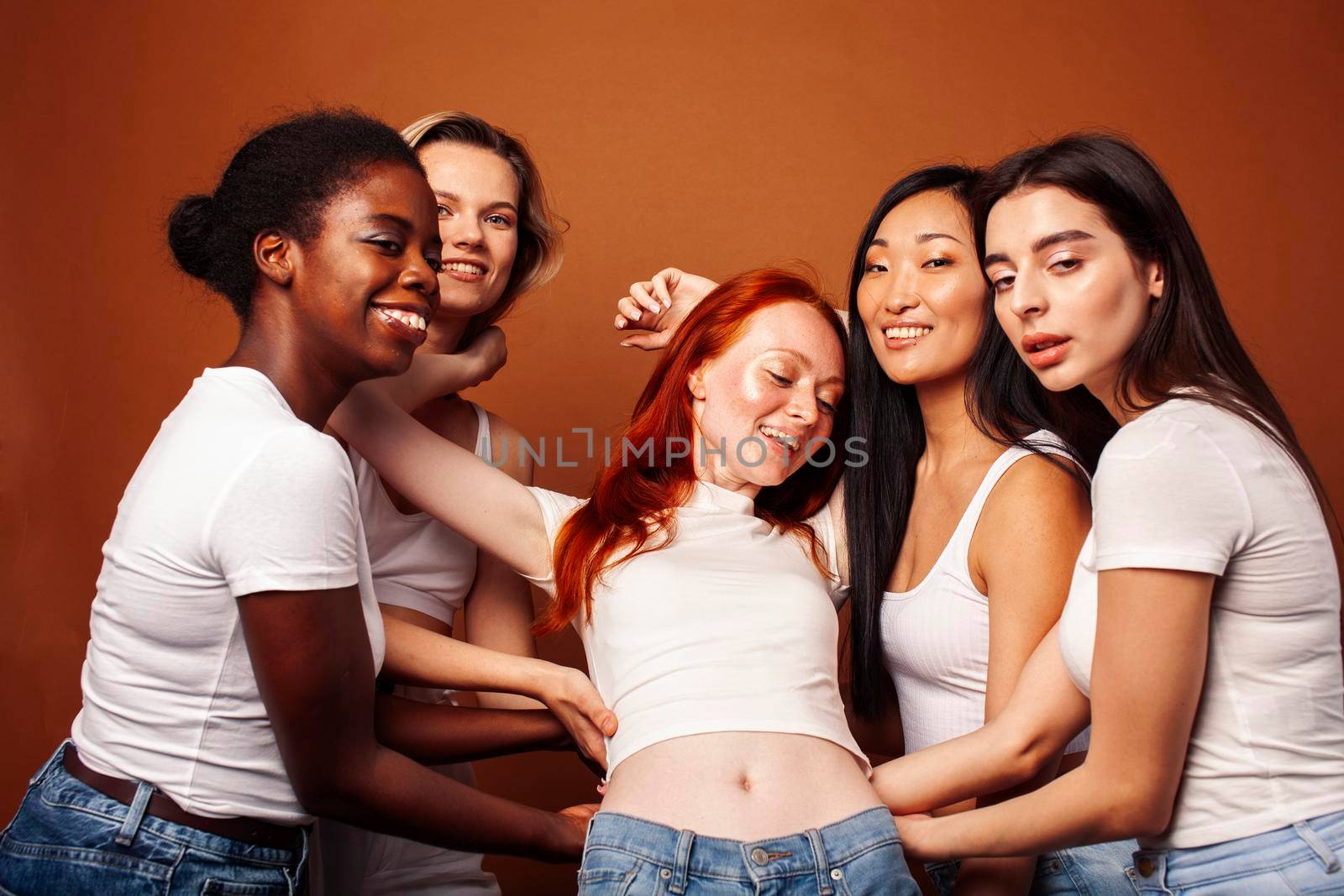 young pretty african and caucasian women posing cheerful together on brown background, lifestyle diverse nationality people concept close up