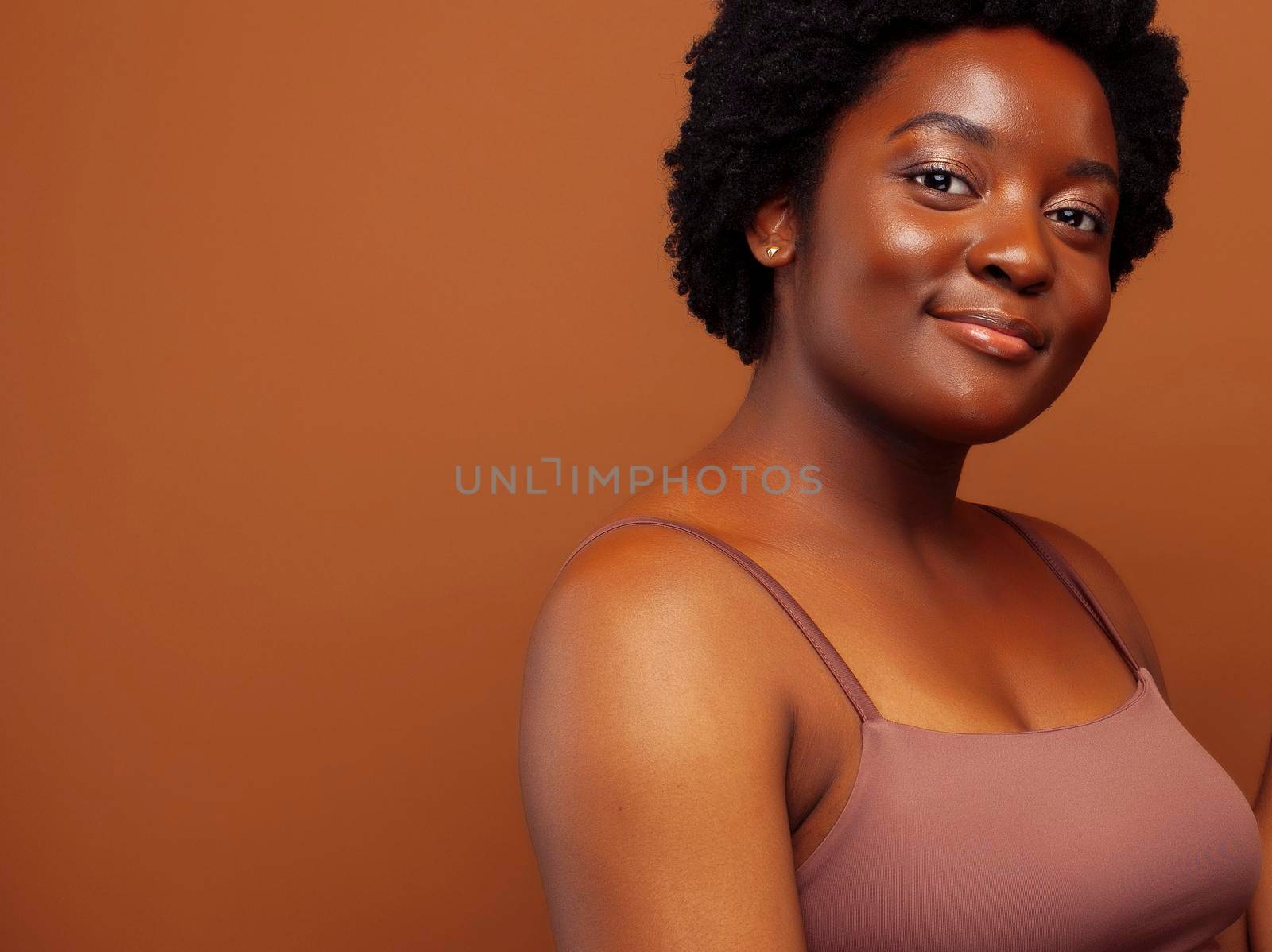 pretty young african american woman with curly hair posing cheerful gesturing on brown background, lifestyle people concept close up