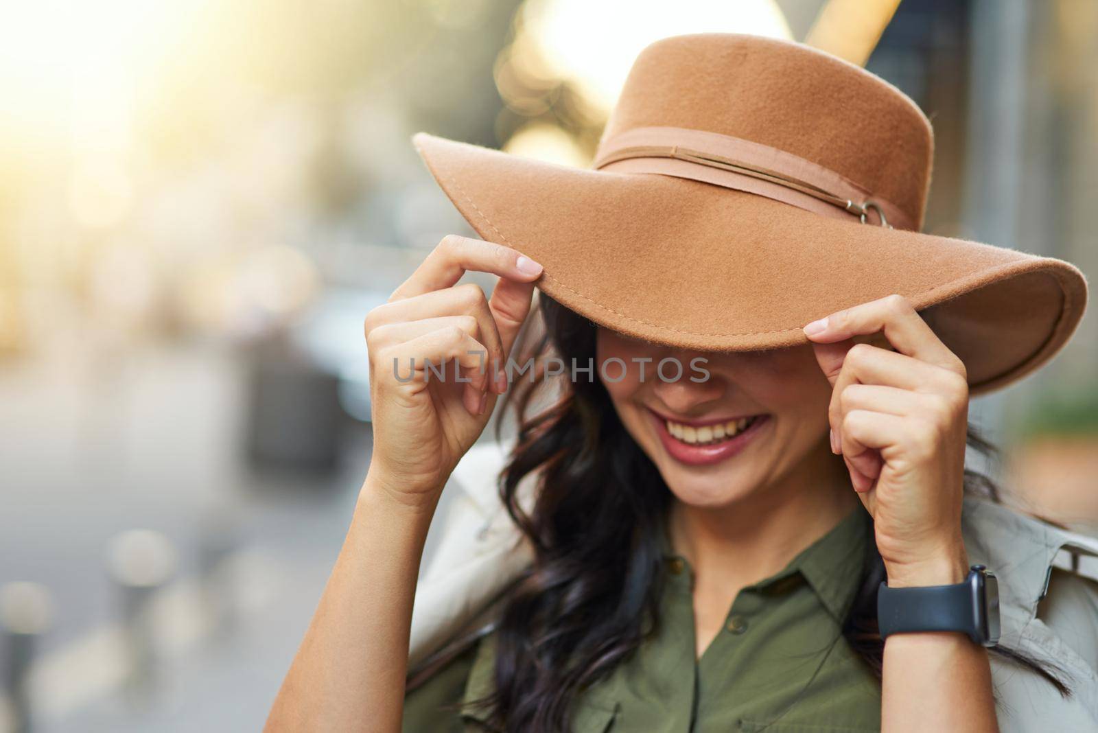 Portrait of a young playful caucasian woman adjusting hat and smiling while walking on warm autumn day by friendsstock