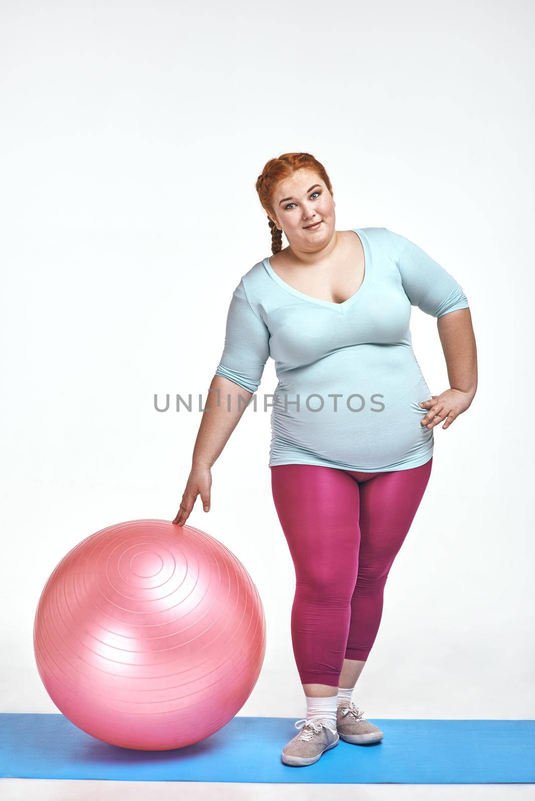 Funny picture of amusing, red haired, chubby woman on white background. Woman holding a ball
