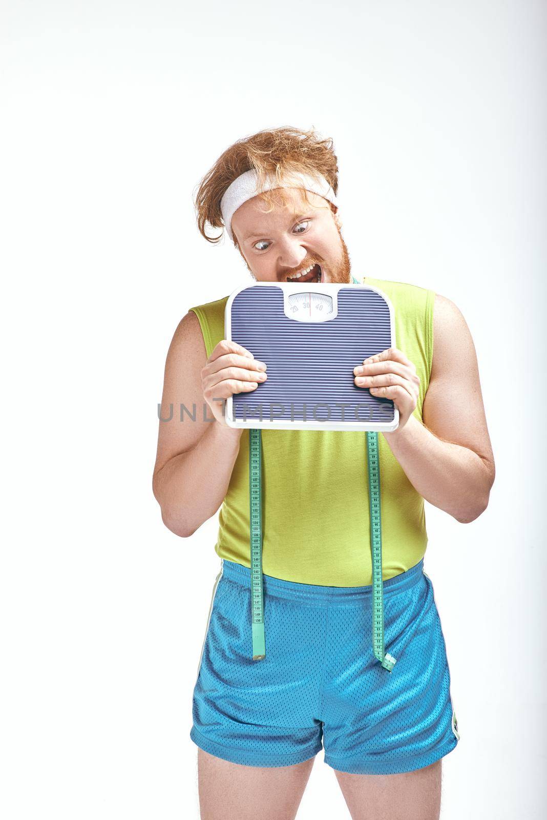 Funny picture of red haired, bearded, plump man on white background. Man holding the scales