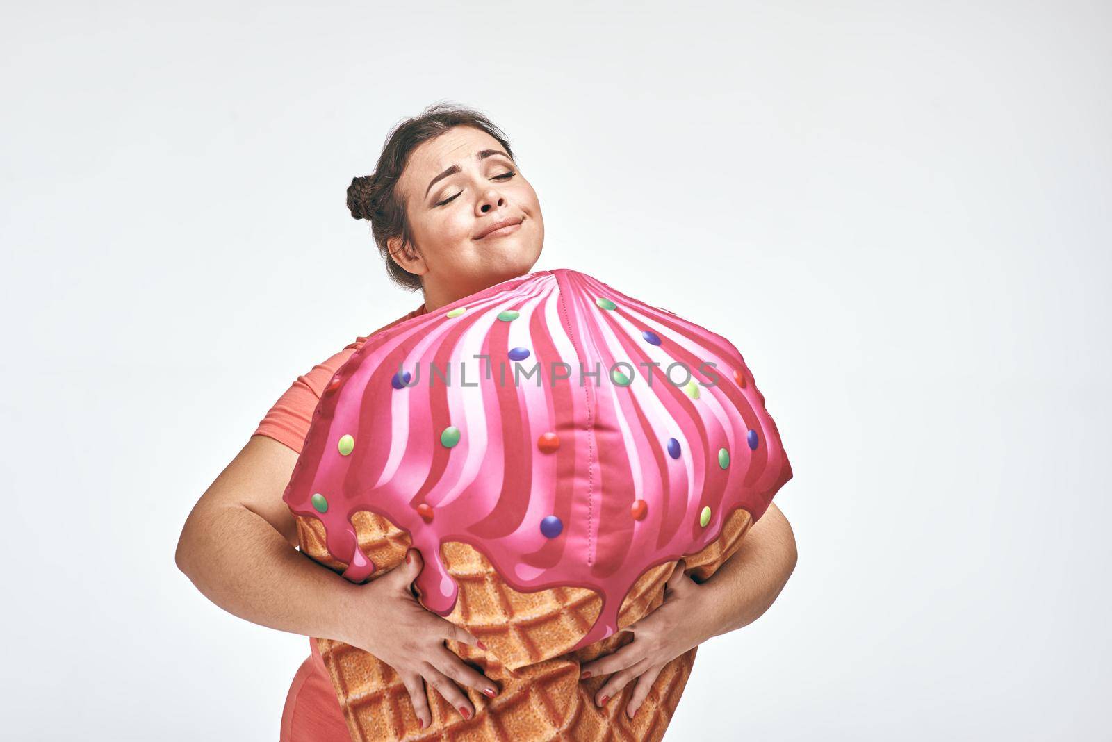 Funny picture of amusing, brunette, chubby woman on white background. Woman is holding a huge ice cream