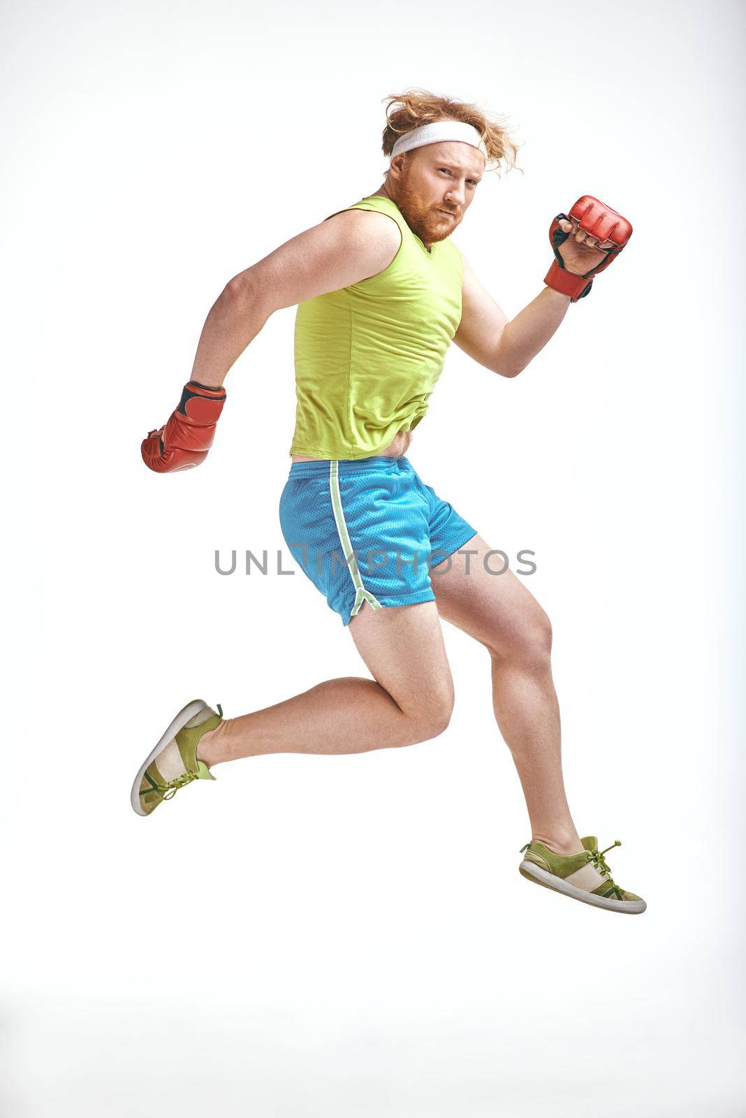 Red haired, bearded, plump man jumps in red boxing gloves by friendsstock