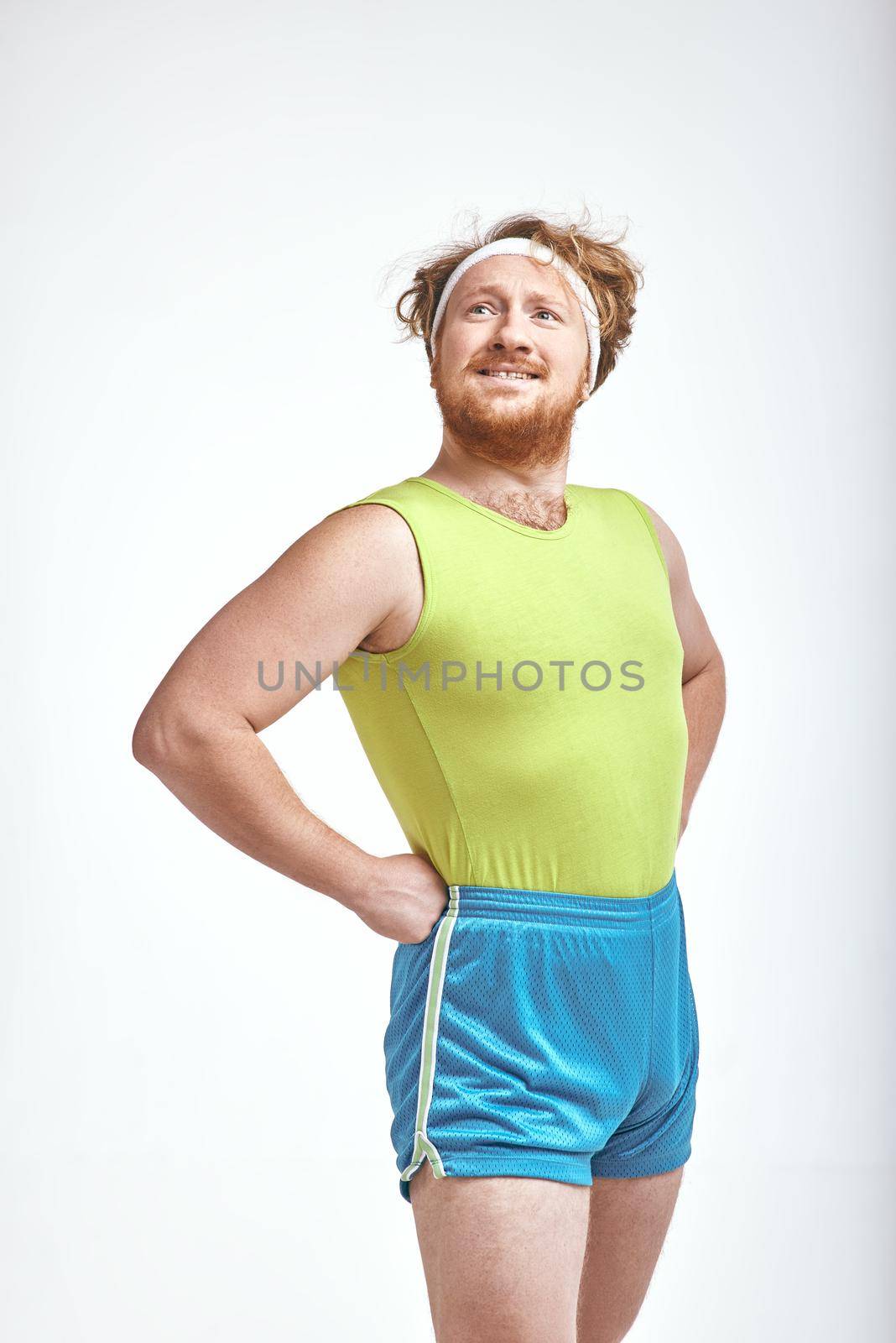 Funny picture of red haired, bearded, plump man on white background. Man wearing sportswear