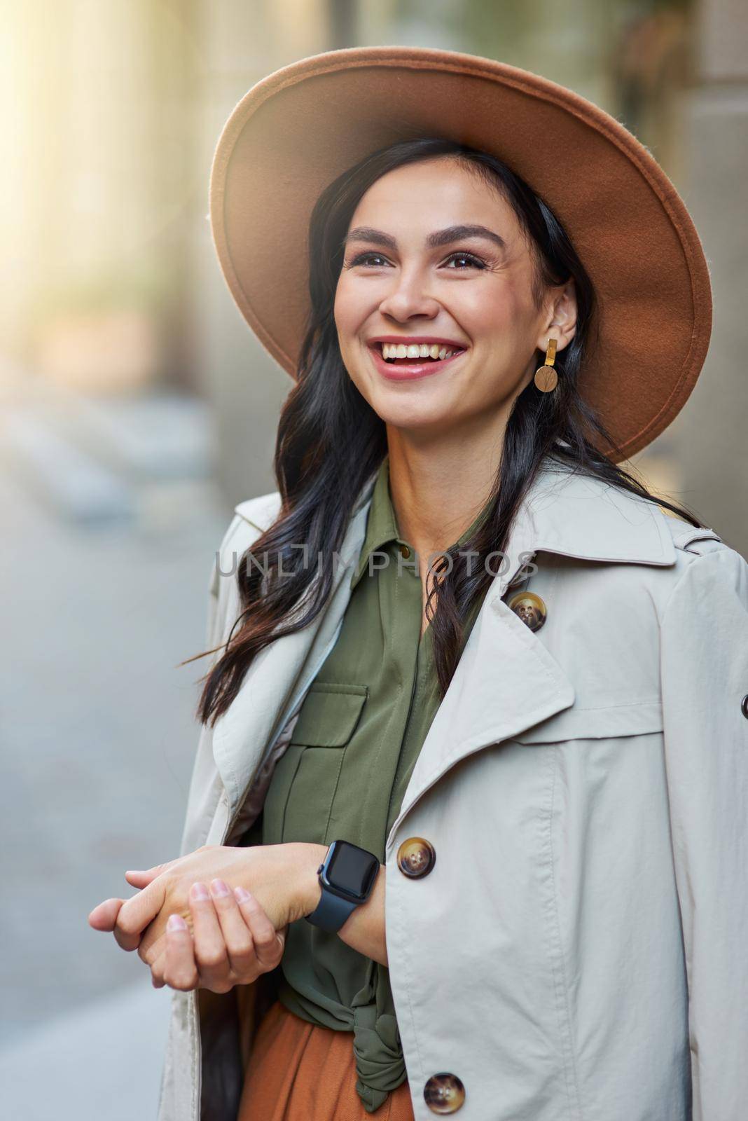 Vertical shot of attractive happy stylish woman wearing grey coat and hat looking aside and smiling while standing on the city street, enjoying walking on warm autumn day by friendsstock