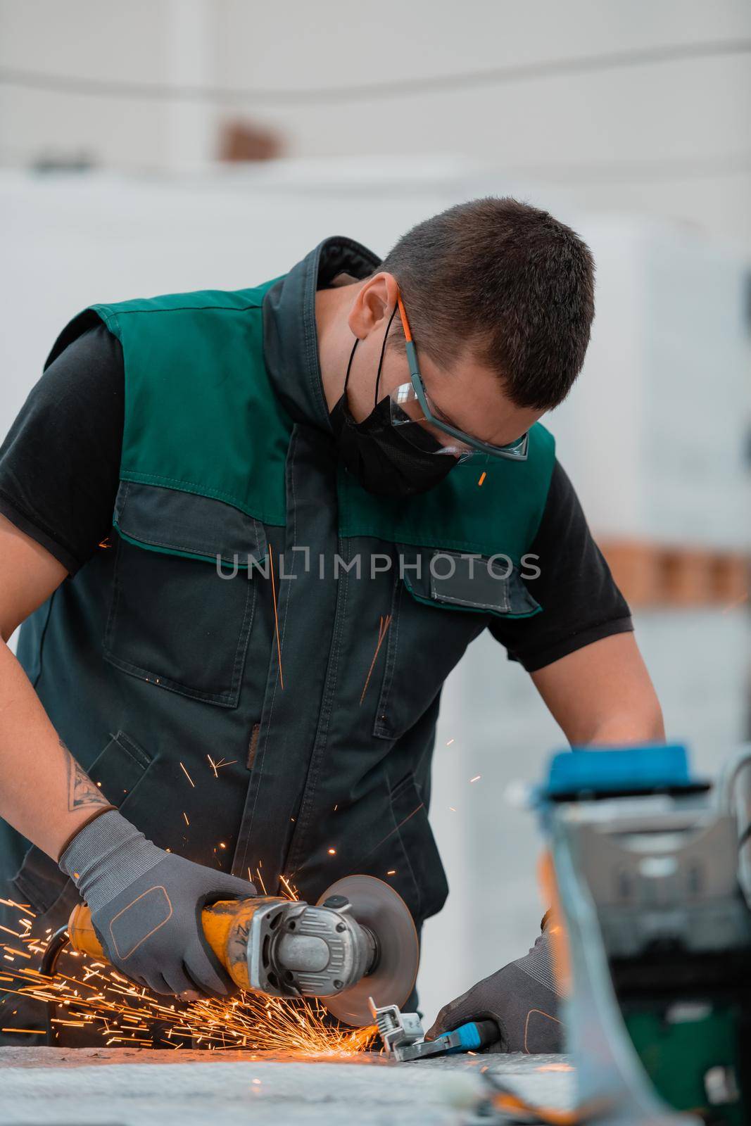 Heavy Industry Engineering Factory Interior with Industrial Worker Using Angle Grinder and Cutting a Metal Tube.He Wears a Mask on His Face Because of the Coronavirus Pandemic. High quality photo