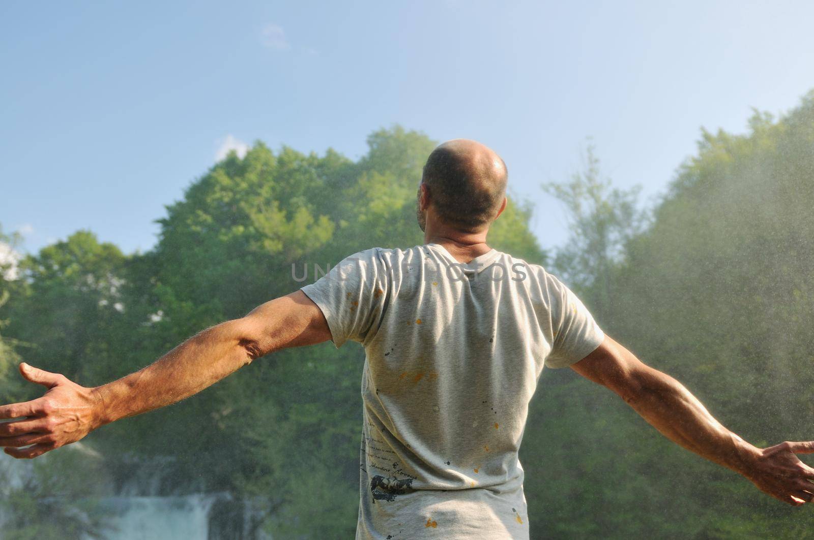 standing man with wide opened arms with waterfalls in background and representing freshness healthy lifestyle and success concept