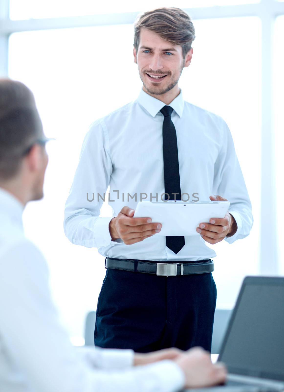 young businessmen communicate in the office. one looks at the tablet. The second one offers ideas on business