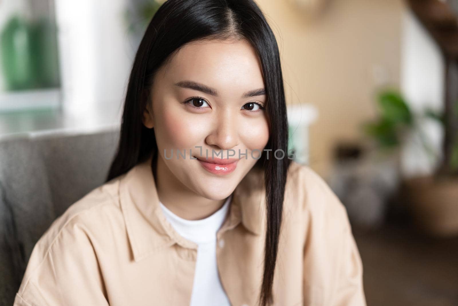 Close up portrait of smiling asian girl looking happy at camera, sitting at home indoors. Face of young woman with joyful emotion.
