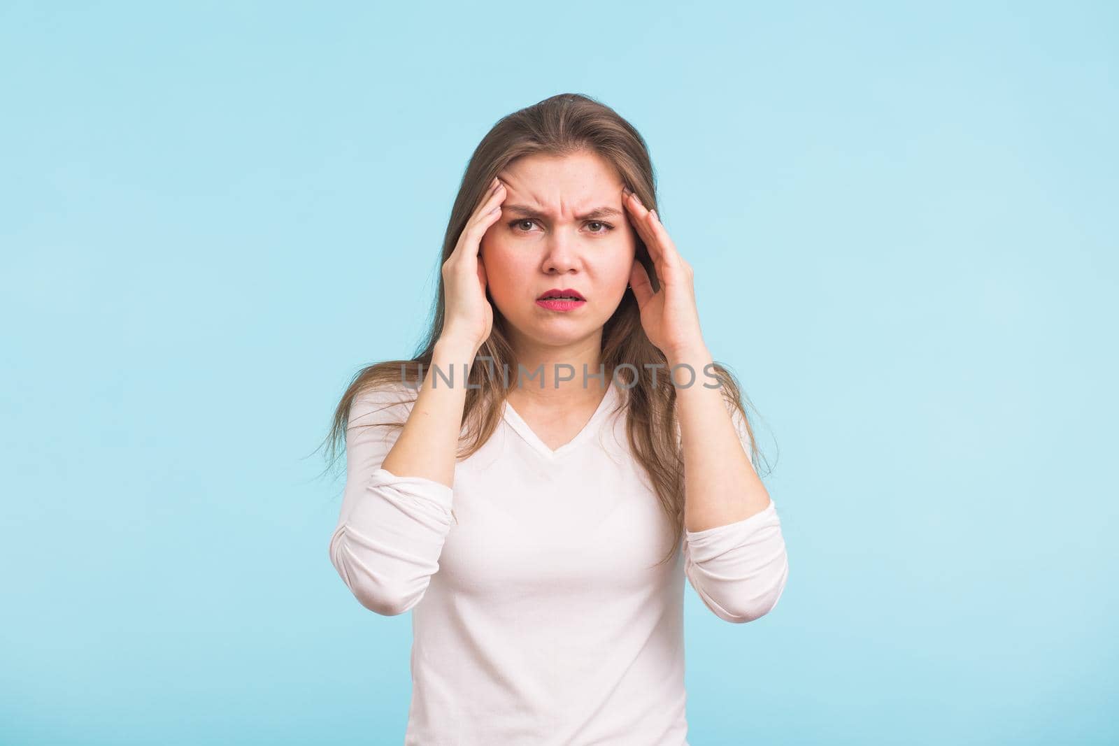 Portrait of beautiful young woman with bare shoulders touching her temples feeling stress, on blue background.