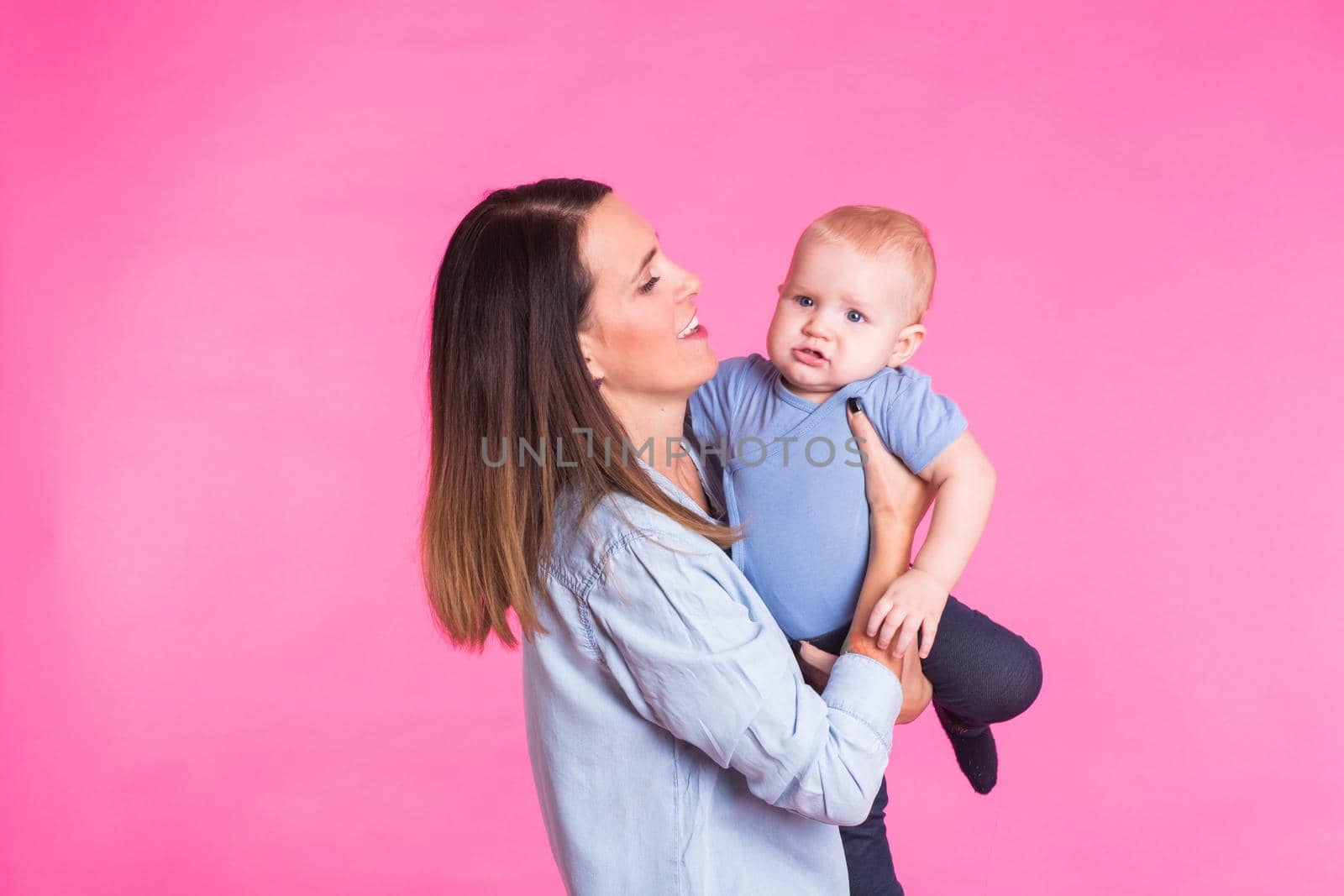 happy young mother with a baby child on pink background.