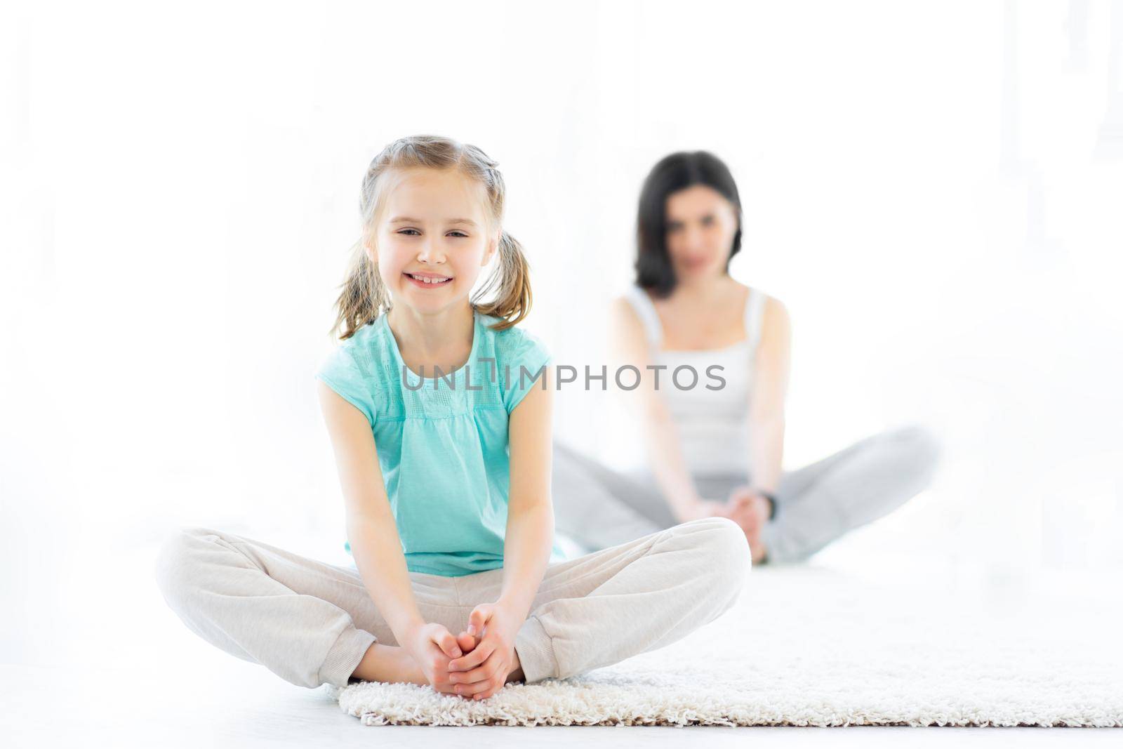 Cute little girl doing sports with mother in light room