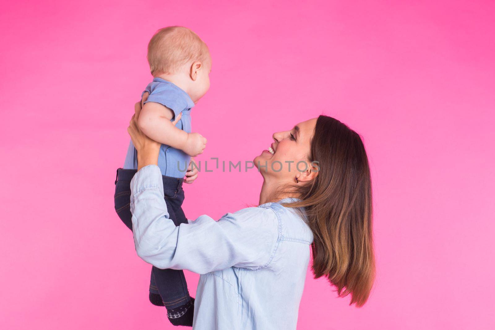 family, motherhood, parenting, people and child care concept - happy mother holds adorable baby over pink background.